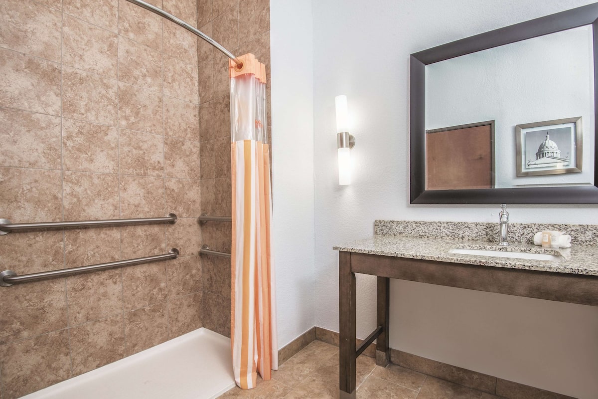 A bathroom with a bathtub, a shower curtain, a sink with a mirror, and a framed picture on the wall.