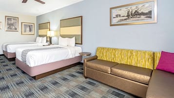 Habitación de hotel con dos camas, un sofá, un ventilador de techo y un cuadro en la pared.