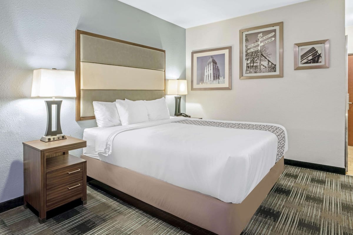 A hotel room with a large bed, two bedside tables with lamps, a headboard, and framed pictures on the wall.