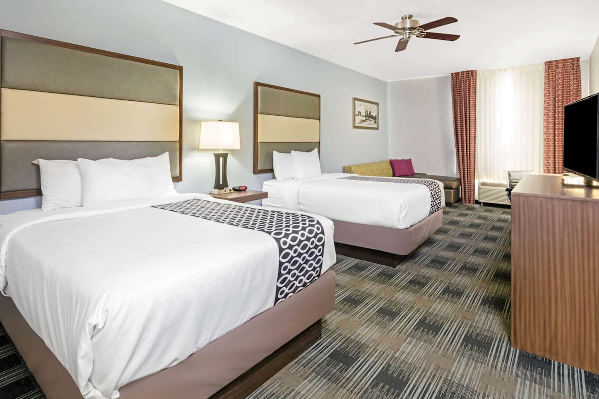 A hotel room with two beds, a ceiling fan, a television, and a desk.