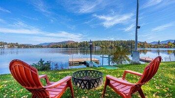 Vista del lago con dos sillas Adirondack, un brasero y un muelle que se adentra en el agua.