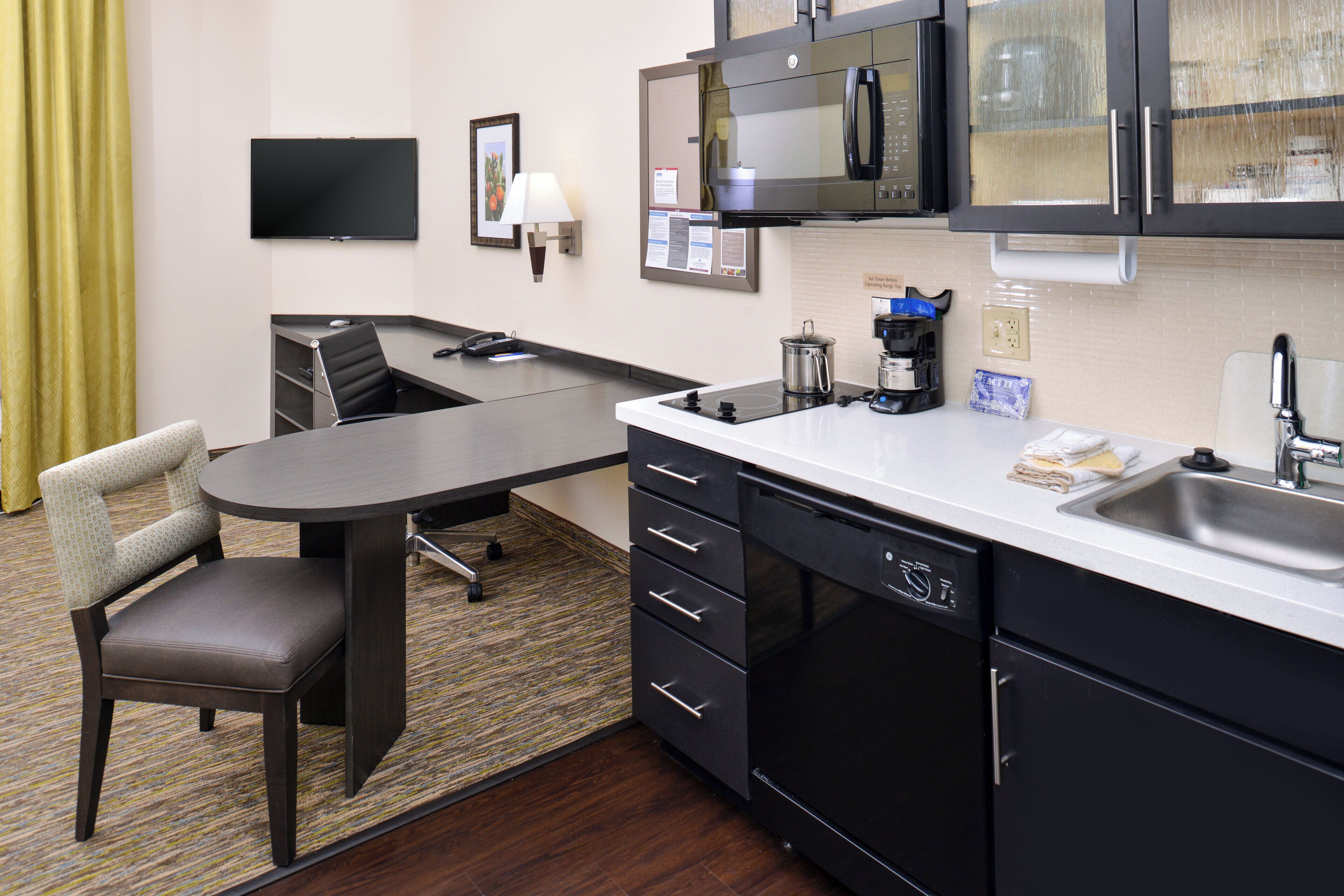 A compact hotel room with a kitchenette, a dining area, a flat-screen TV, and a small seating area.
