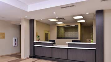 A reception desk with a modern design, a large mirror above it, and a sign indicating the location of the guest laundry and meeting room.