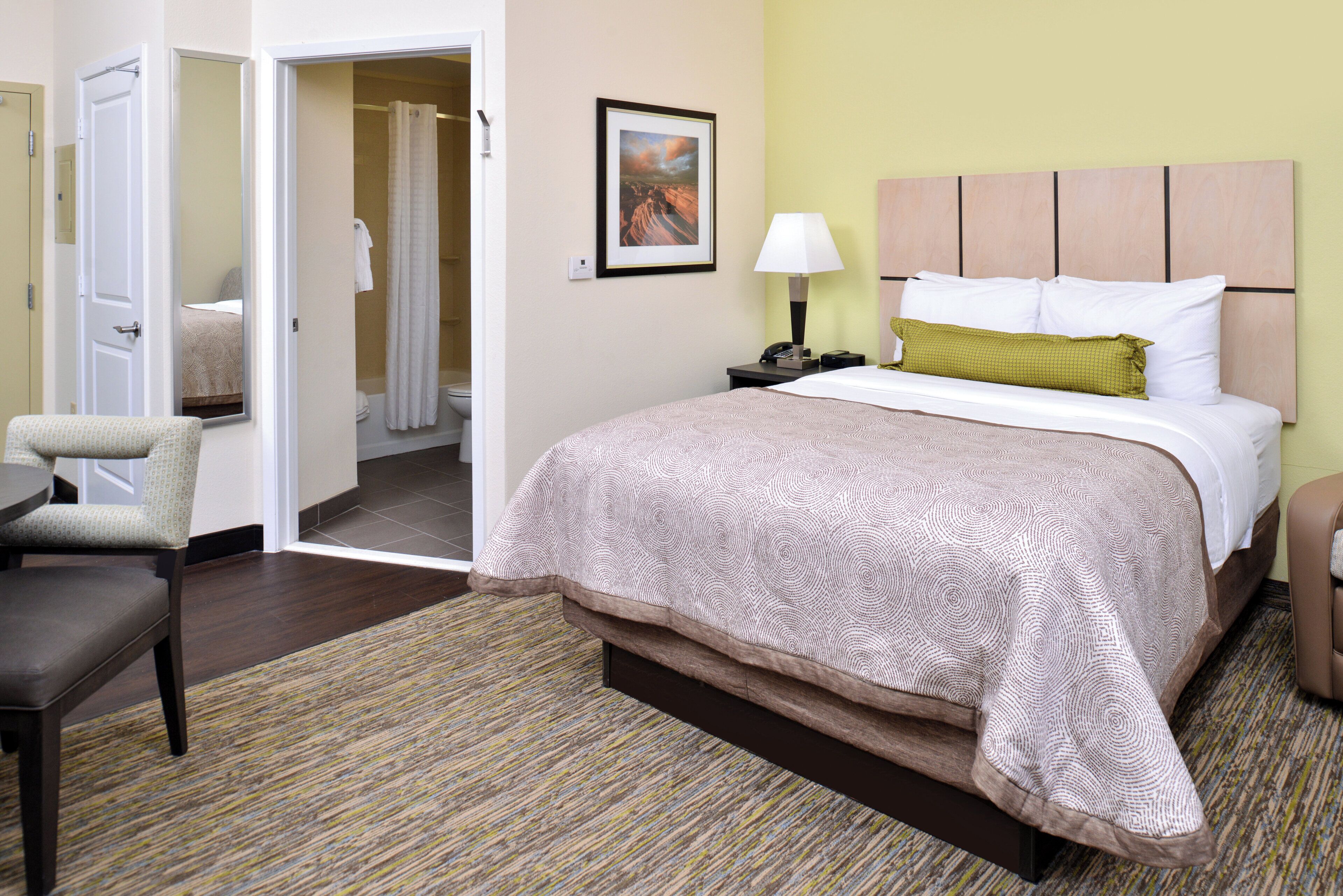 Une chambre d’hôtel comprenant un lit, une chaise, une table de chevet avec une lampe et une porte donnant accès à une salle de bain.