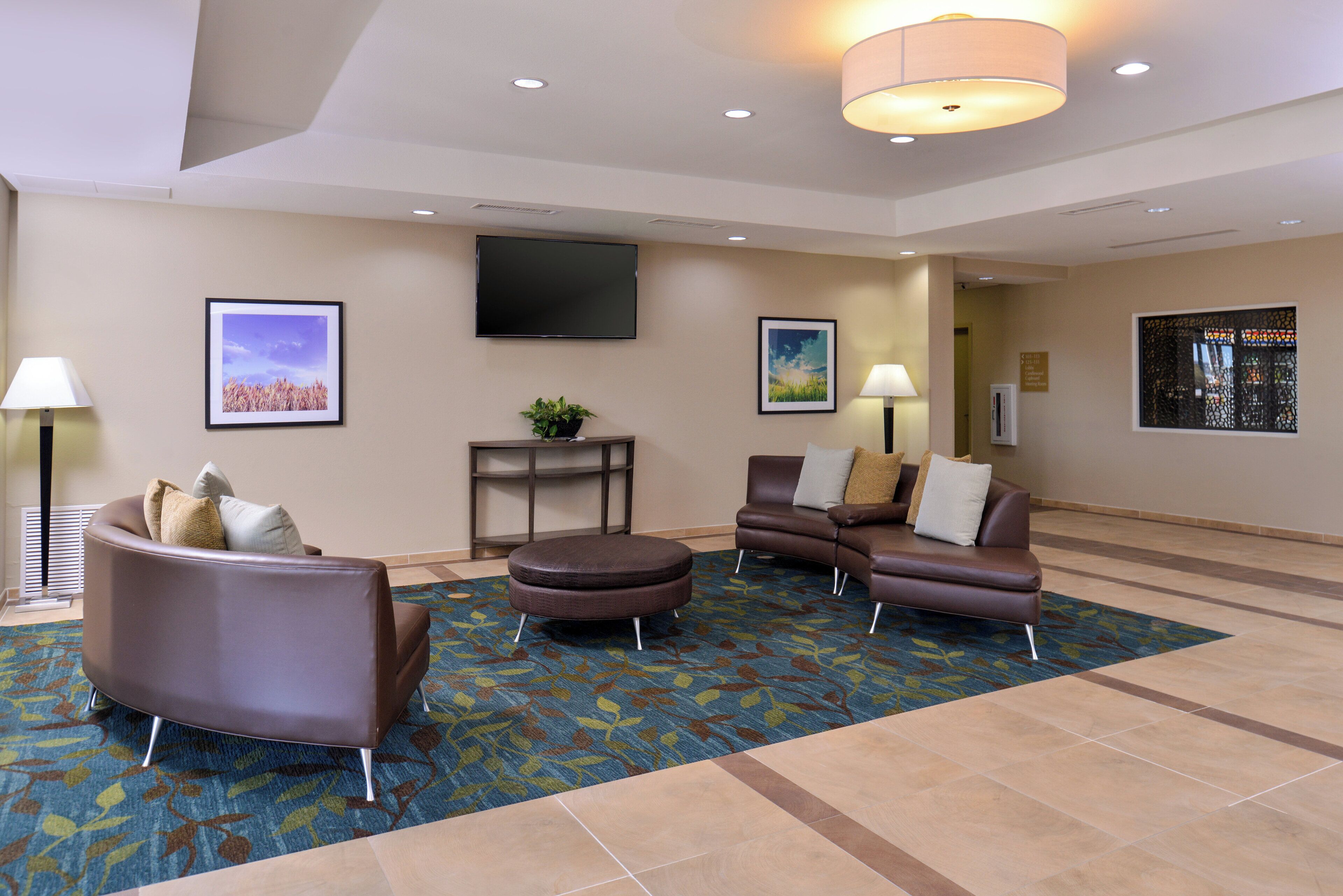 A hotel lobby with a seating area, a flat-screen TV mounted on the wall, and a reception desk.