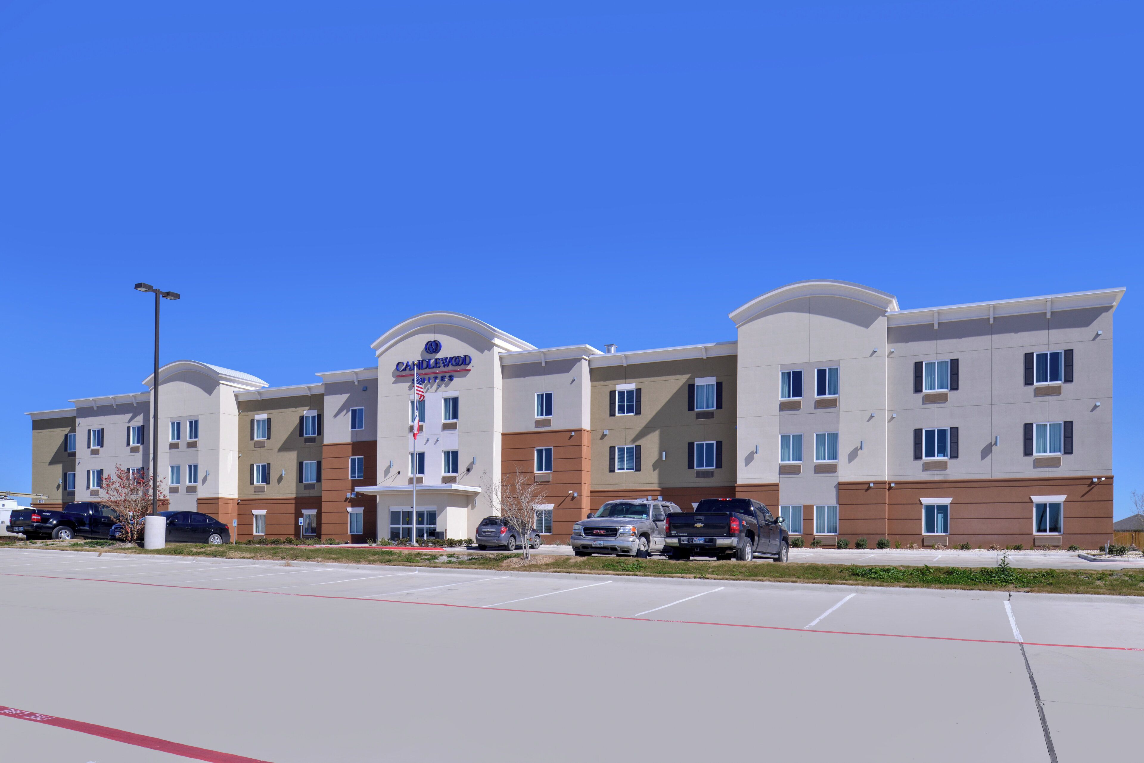 A multi-story hotel with a prominent American flag, parking lot, and several vehicles.