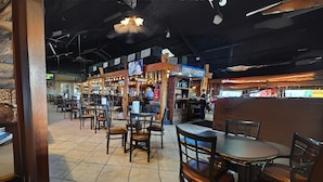 An indoor restaurant with wooden tables and chairs, a bar area, and a ceiling fan. - Candlewood Suites Kenedy by IHG (Kenedy)