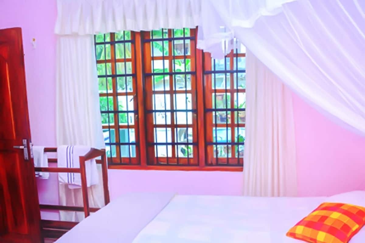 A room with a bed, a window with a view of greenery, a chair, and a door.