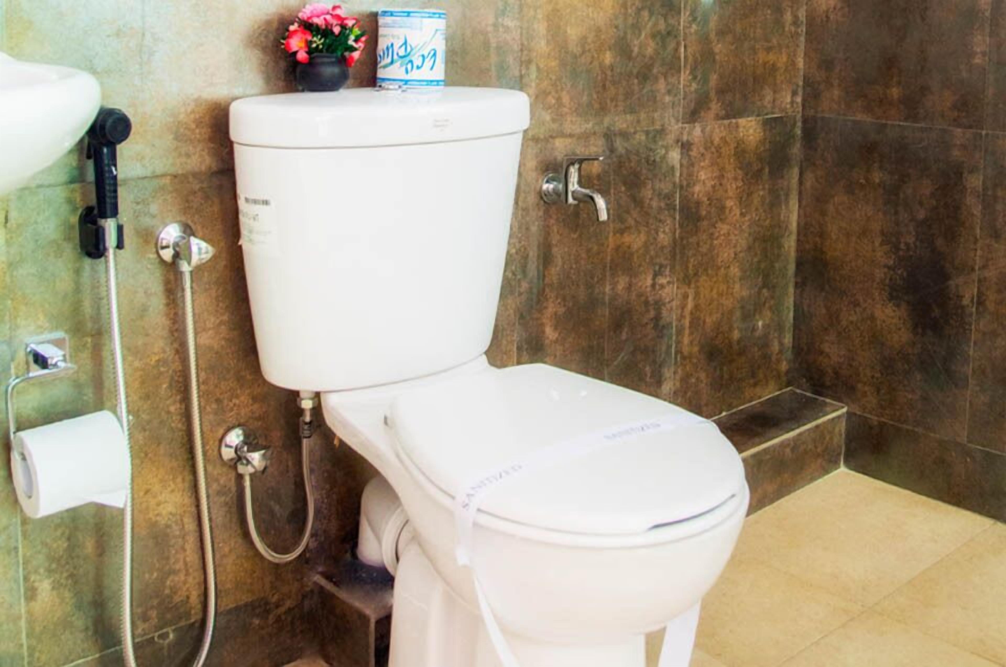 A toilet with a tank, a bidet attachment, and a toilet paper holder.