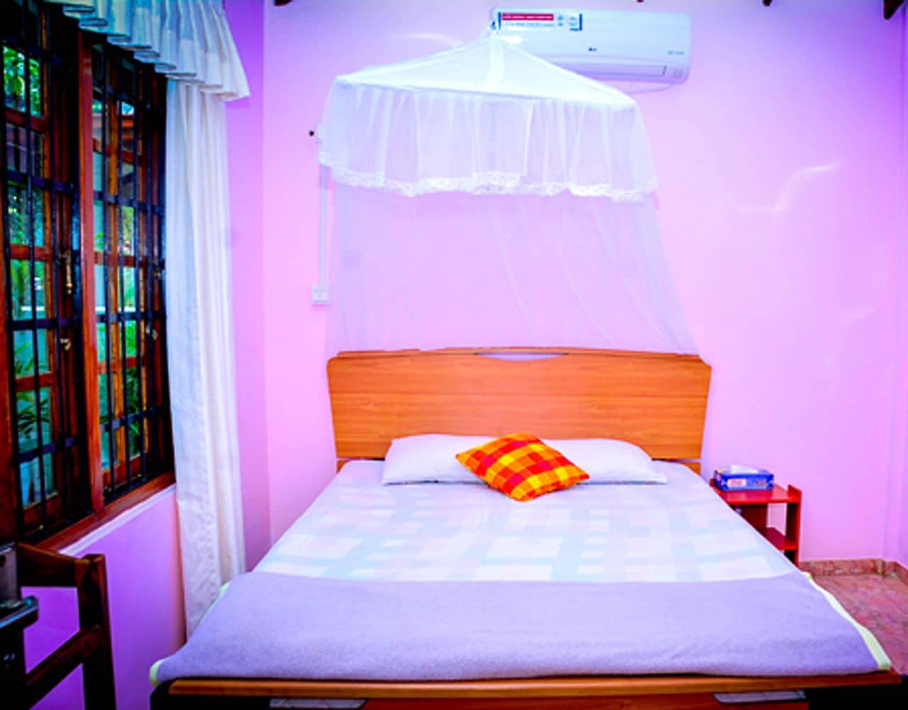 Una cama con cabecera de madera, mosquitero blanco y almohada colorida.