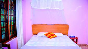 Una cama con cabecera de madera, mosquitero blanco y almohada colorida.
