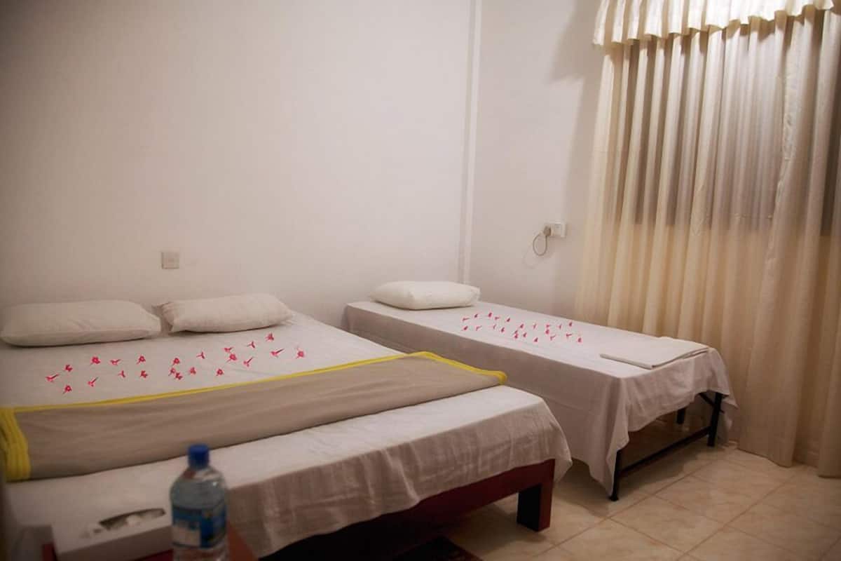 A room with two single beds, each with a white bedspread and pillows. There is a water bottle on the floor near one bed.