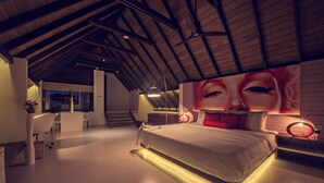 A modern bedroom with a large bed, a desk, and a chair. There is a staircase leading to an upper level. - Pledge3 (Negombo)
