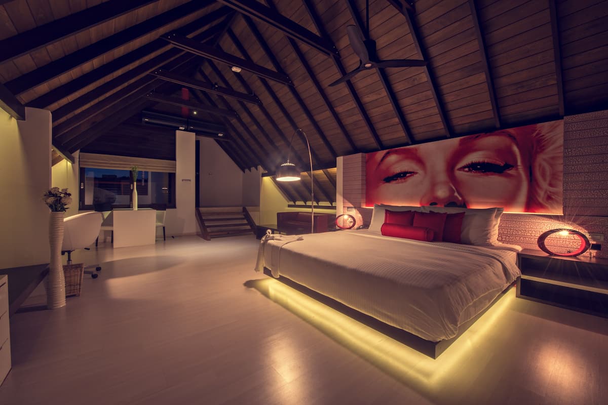 Ein modernes Schlafzimmer mit einem großen Bett, einem Schreibtisch und einem Stuhl. Eine Treppe führt zu einer oberen Ebene.