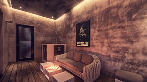 A modern, cozy room with a wooden floor, a wicker sofa, a white side table, and a small white ottoman. - Pledge3 (Negombo)