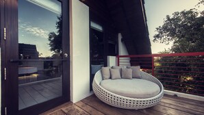 A modern outdoor seating area with a round, woven design, a cushioned bench, and a glass door leading to a deck. - Pledge3 (Negombo)
