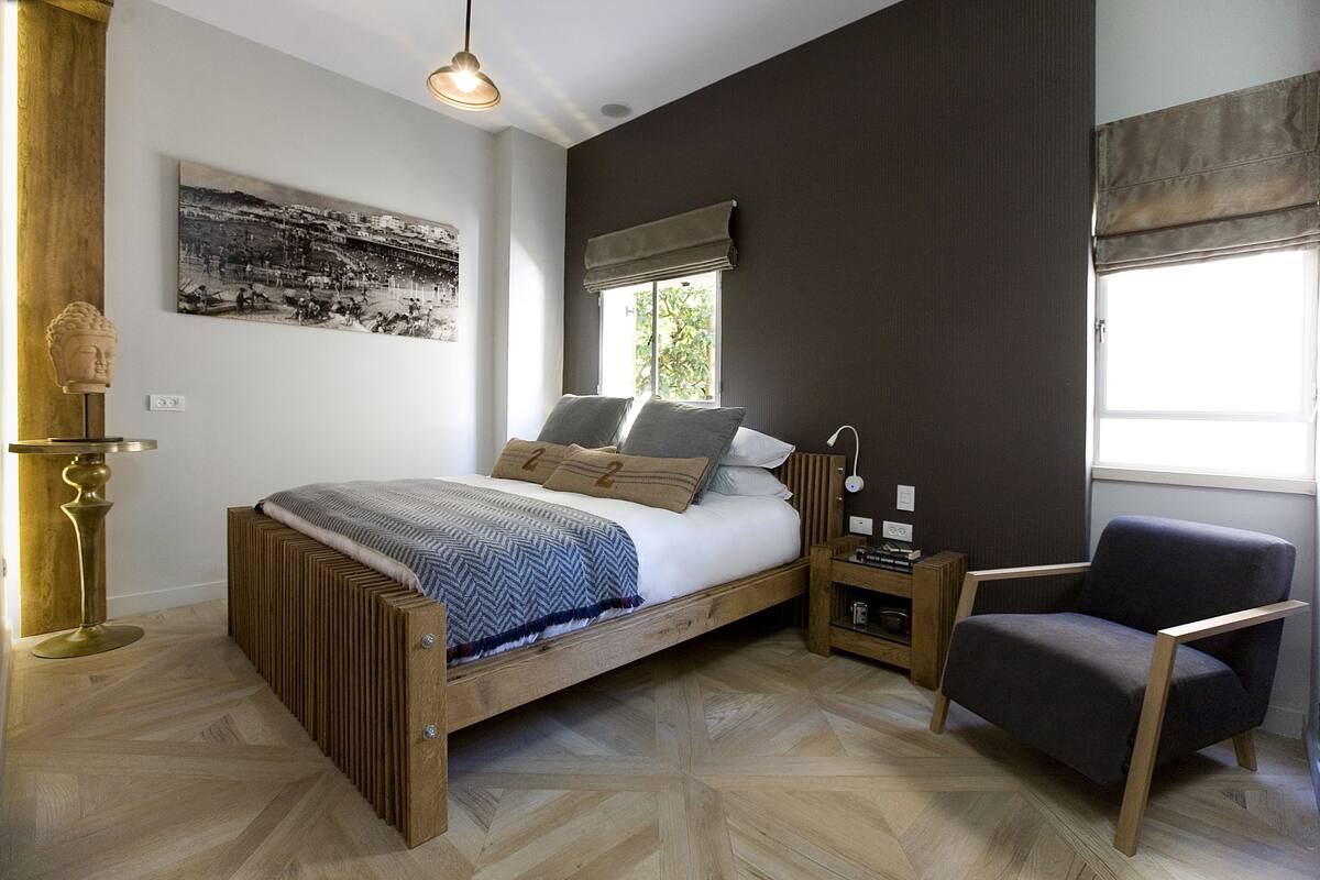 A bedroom with a bed, a chair, a nightstand, a lamp, a window with curtains, and a wall-mounted picture.