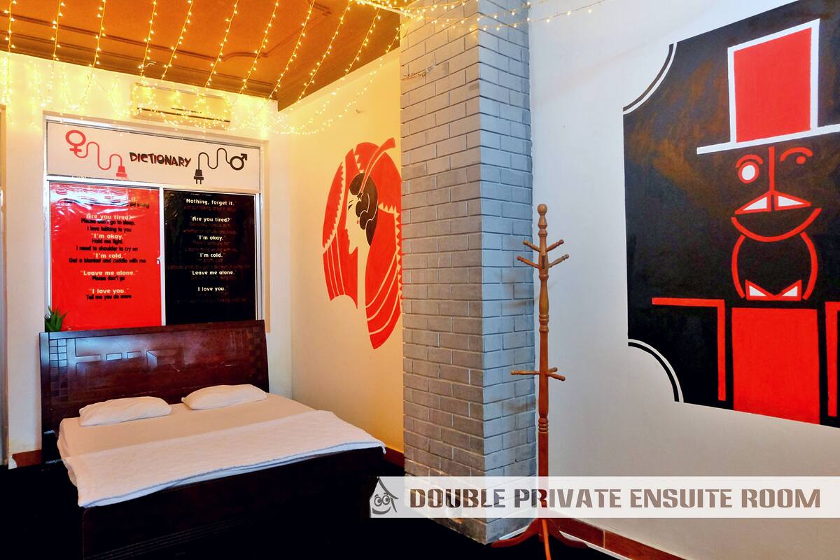 Ein privates Doppelzimmer mit eigenem Bad, einem Bett, einem wandmontierten Wörterbuch und einem einzigartigen abstrakten Kunstwerk.