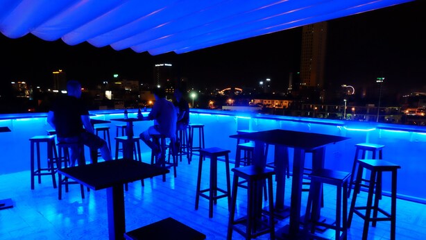 A rooftop bar with tables and stools, overlooking a cityscape at night. - Danang Backpackers Hostel (Da Nang)