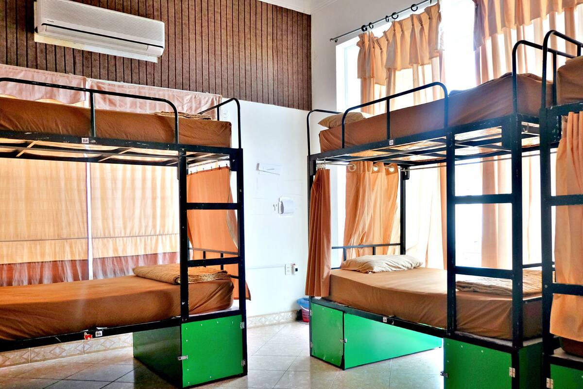 Ein Schlafsaalzimmer mit Etagenbetten, einem Fenster mit Vorhängen und einer Klimaanlage.
