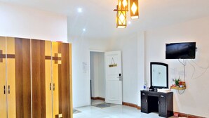 A hotel room with a wardrobe, a door labeled "TRIPLE ROOM", a desk with a mirror, and a TV mounted on the wall. - Danang Backpackers Hostel (Da Nang)