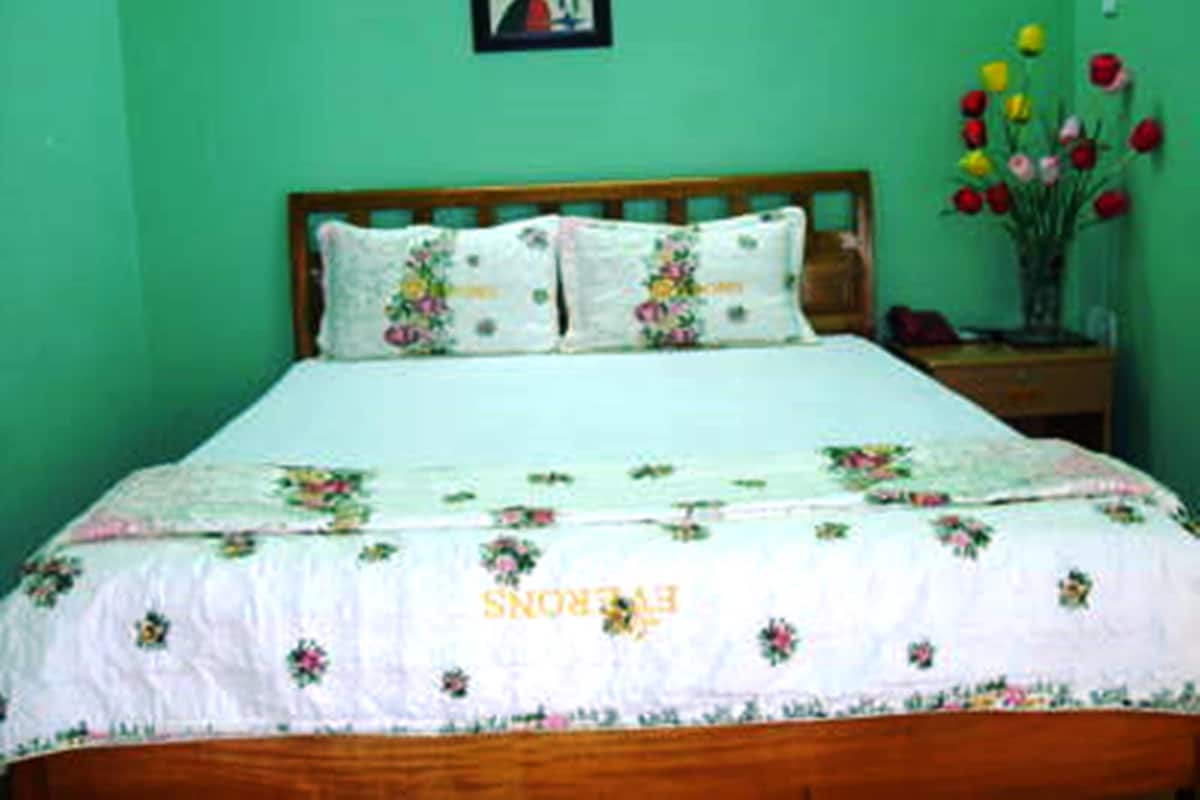 A bedroom with a bed, floral bedding, a nightstand, and a vase of tulips.