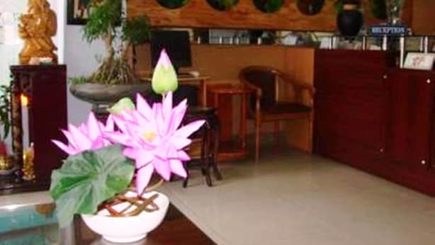 A reception area with a wooden wall, a reception desk, and a potted plant with pink flowers. - Phu My Hotel (Da Nang)