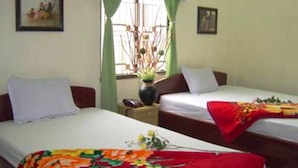 A hotel room with two single beds, a window with green curtains, and a vase with flowers on the nightstand. - Phu My Hotel (Da Nang)