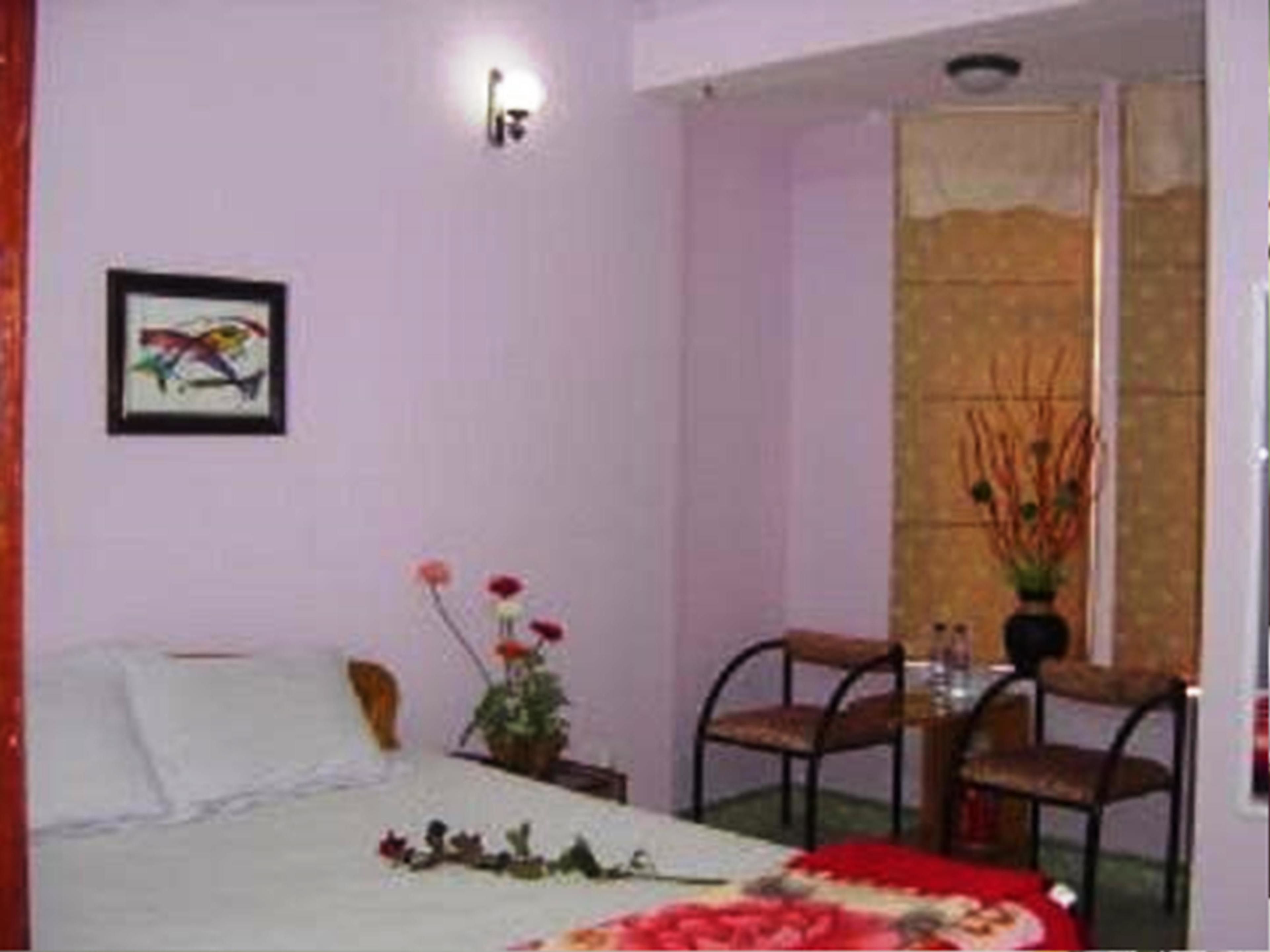 Habitación de hotel con cama, una silla, una mesita con un jarrón de flores y una lámpara de pared.