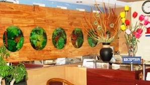 A reception area with a wooden reception desk, a chair, a vase with flowers, and a wall with circular mirrors. - Phu My Hotel (Da Nang)