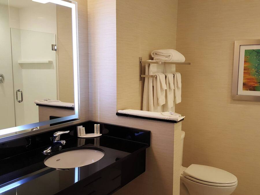 Een moderne badkamer met een zwart wastafel, een spiegel, een toilet en een handdoekrek met opgevouwen handdoeken.