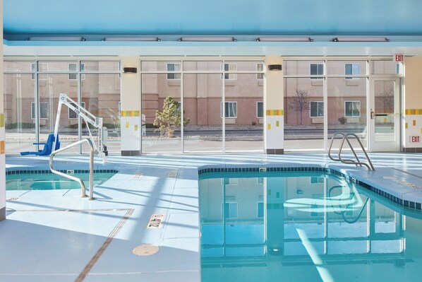 A pool area with clear glass walls, a blue pool, and a metal ladder.