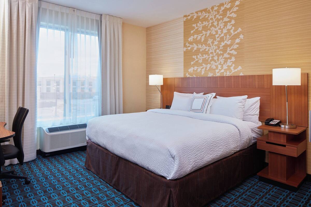 Una habitación de hotel con una cama grande, dos lámparas de noche, un escritorio y una silla.