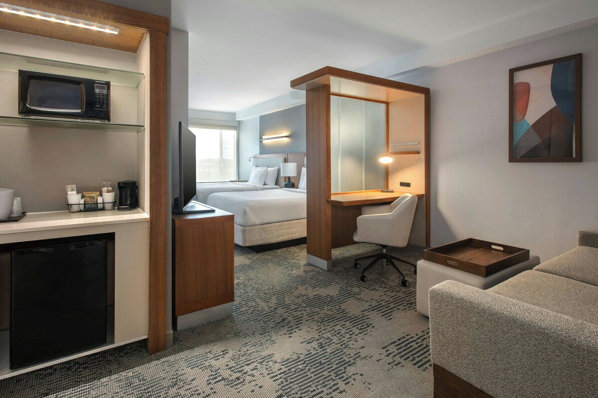 A hotel room with a kitchenette, a bed, a desk, and a chair.