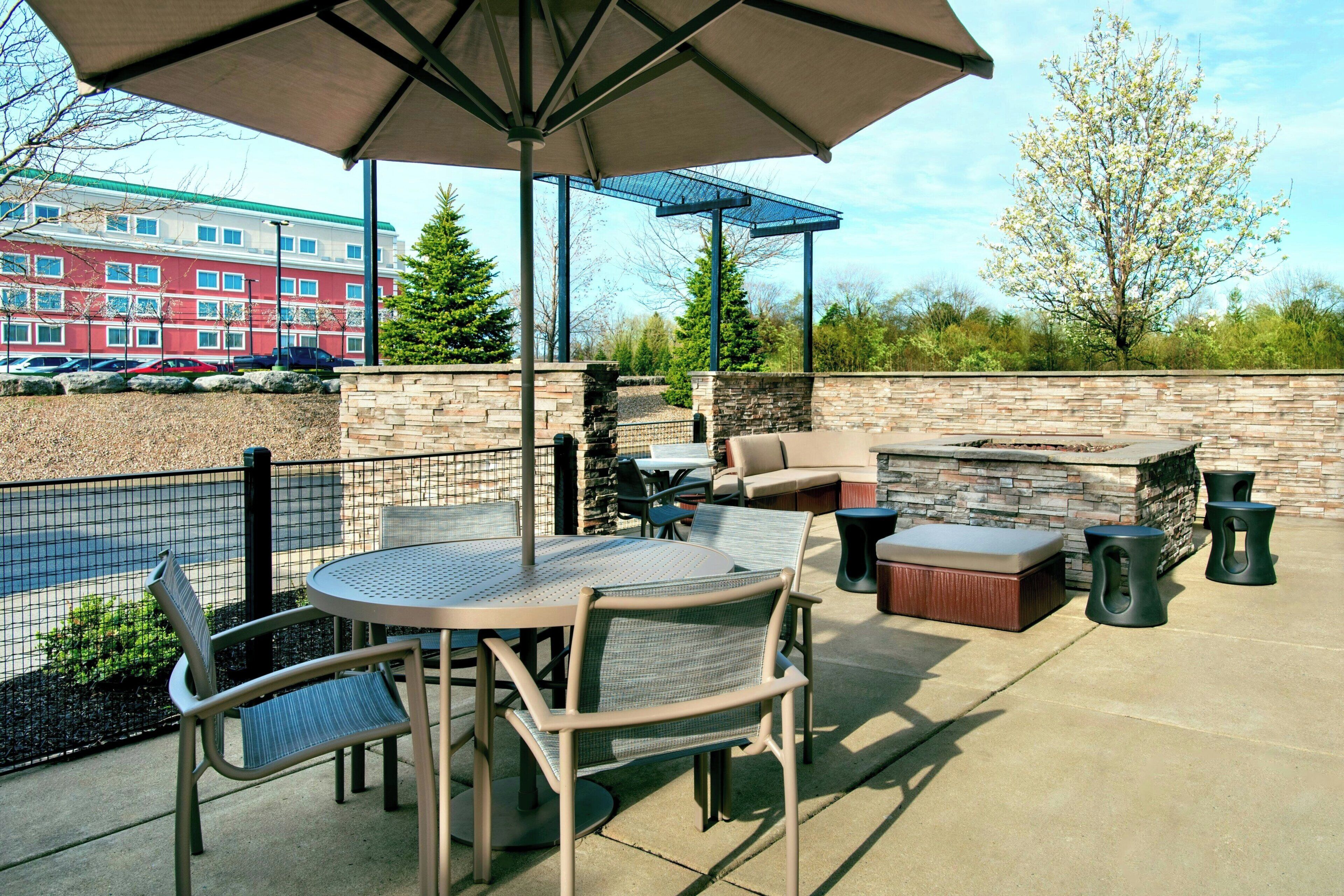 An outdoor patio with a round table, chairs, a cushioned seating area, and a barbecue grill.