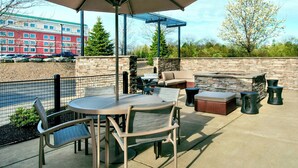 An outdoor patio with a round table, chairs, a cushioned seating area, and a barbecue grill. - Springhill Suites Buffalo Airport (Buffalo)
