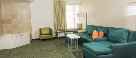 A hotel room with a bathtub, a green sofa, a small table, and a window with curtains.