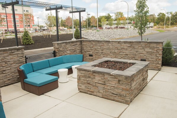 An outdoor patio area with a stone fire pit and a blue sectional sofa. - Springhill Suites Buffalo Airport (Buffalo)