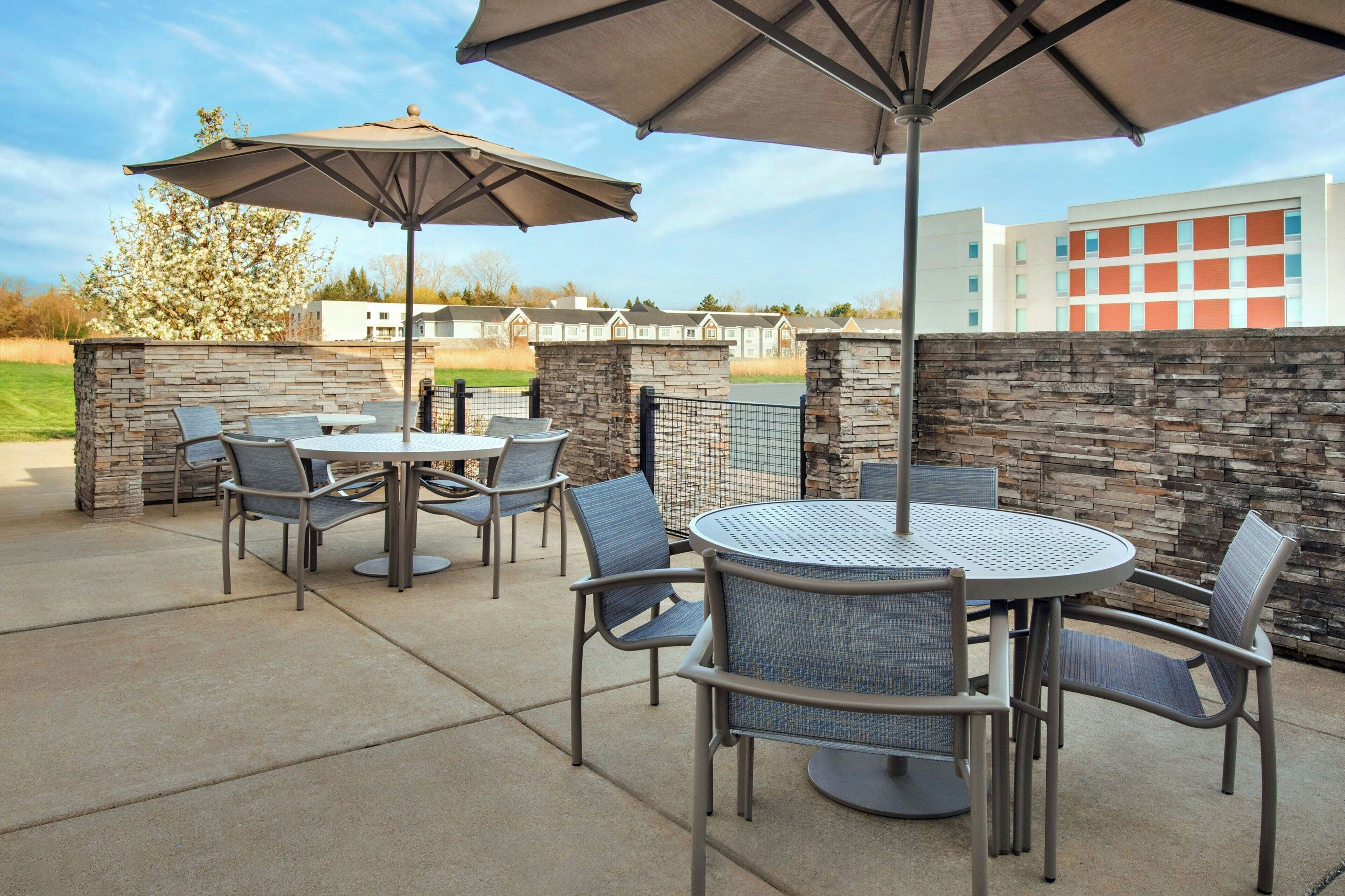 An outdoor patio with stone walls, metal chairs, and round tables under umbrellas.