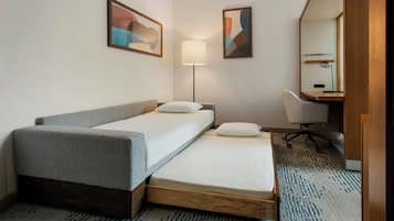 A hotel room with a bed, a desk, a chair, a lamp, and two abstract paintings on the wall.