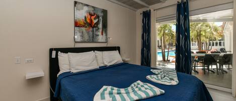 A hotel room with a large bed, a painting on the wall, and a view of the pool and outdoor seating area.