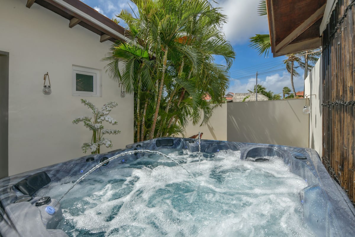 A hot tub with water flowing, surrounded by a white wall and palm trees.