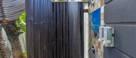 A shower enclosure with a bamboo fence, a wall-mounted control panel, and a palm tree in the background.