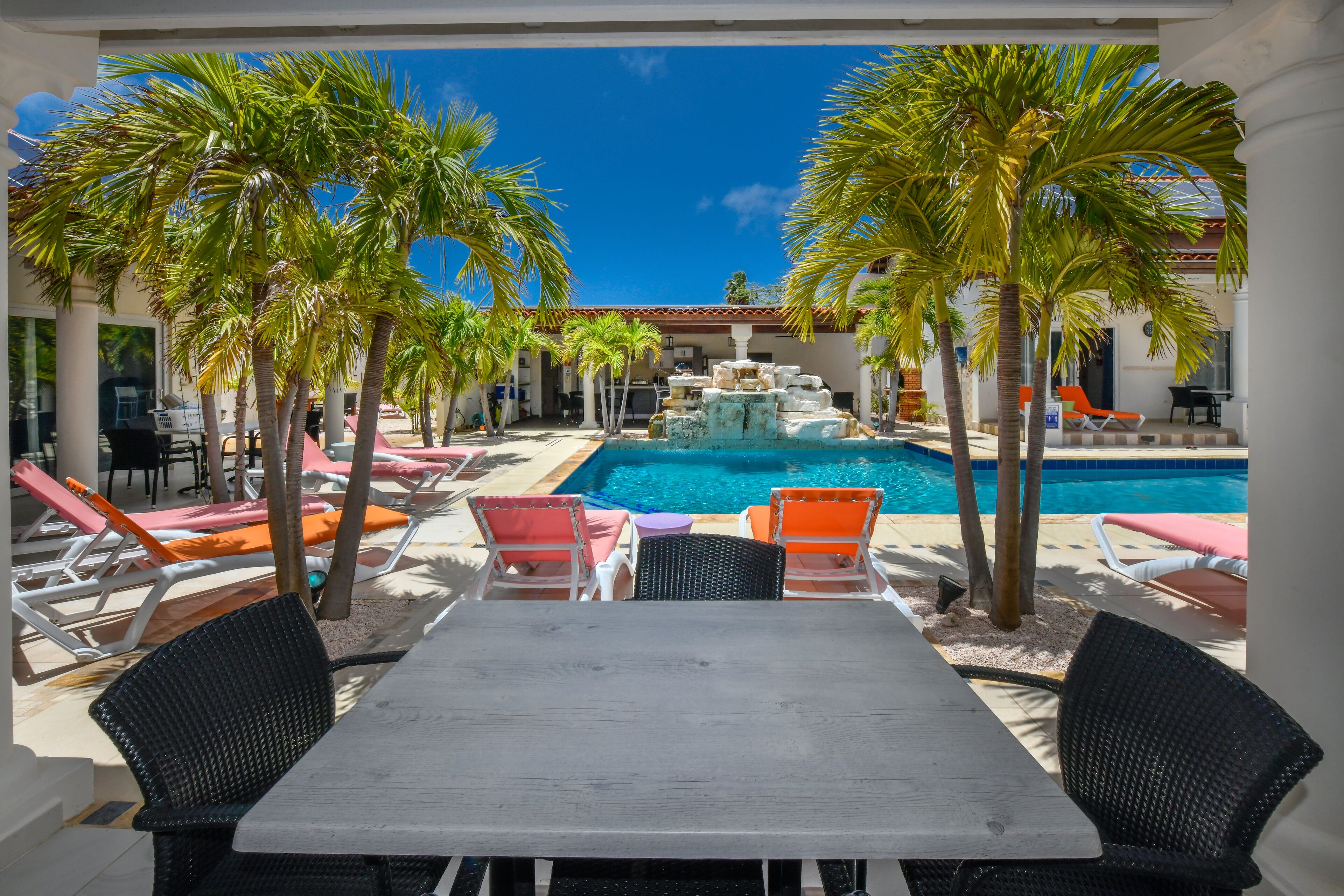 A poolside area with lounge chairs, a table, and palm trees.