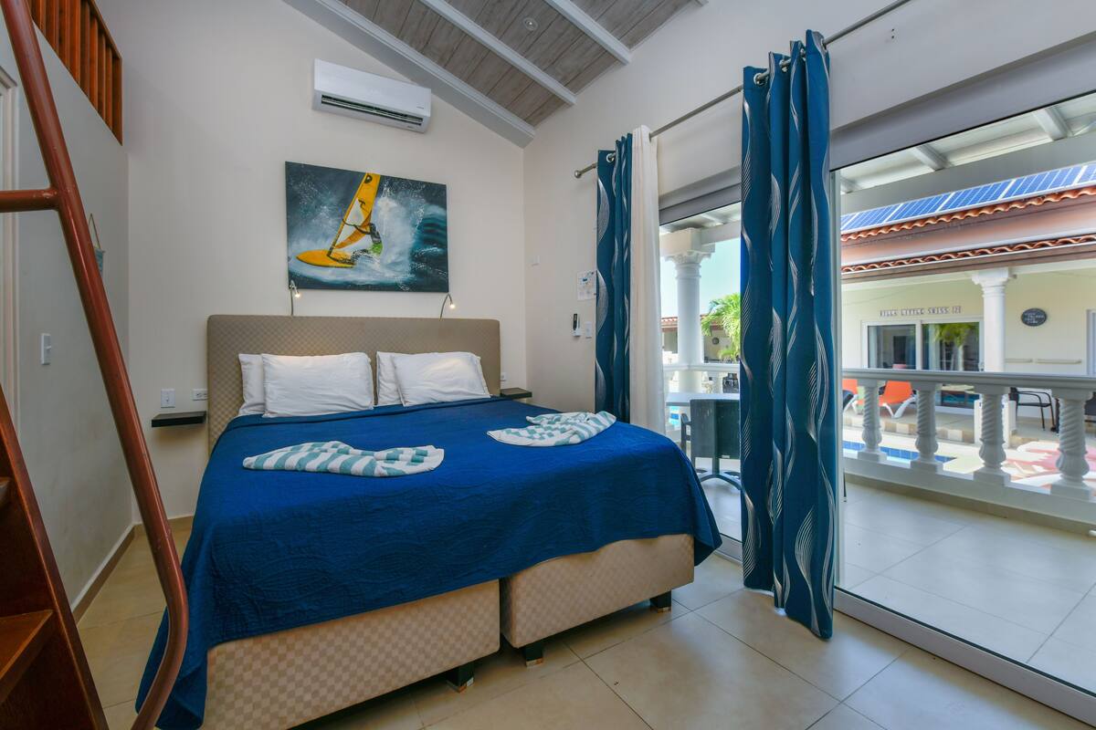 A hotel room with a bed, a painting, and a view of the outside.