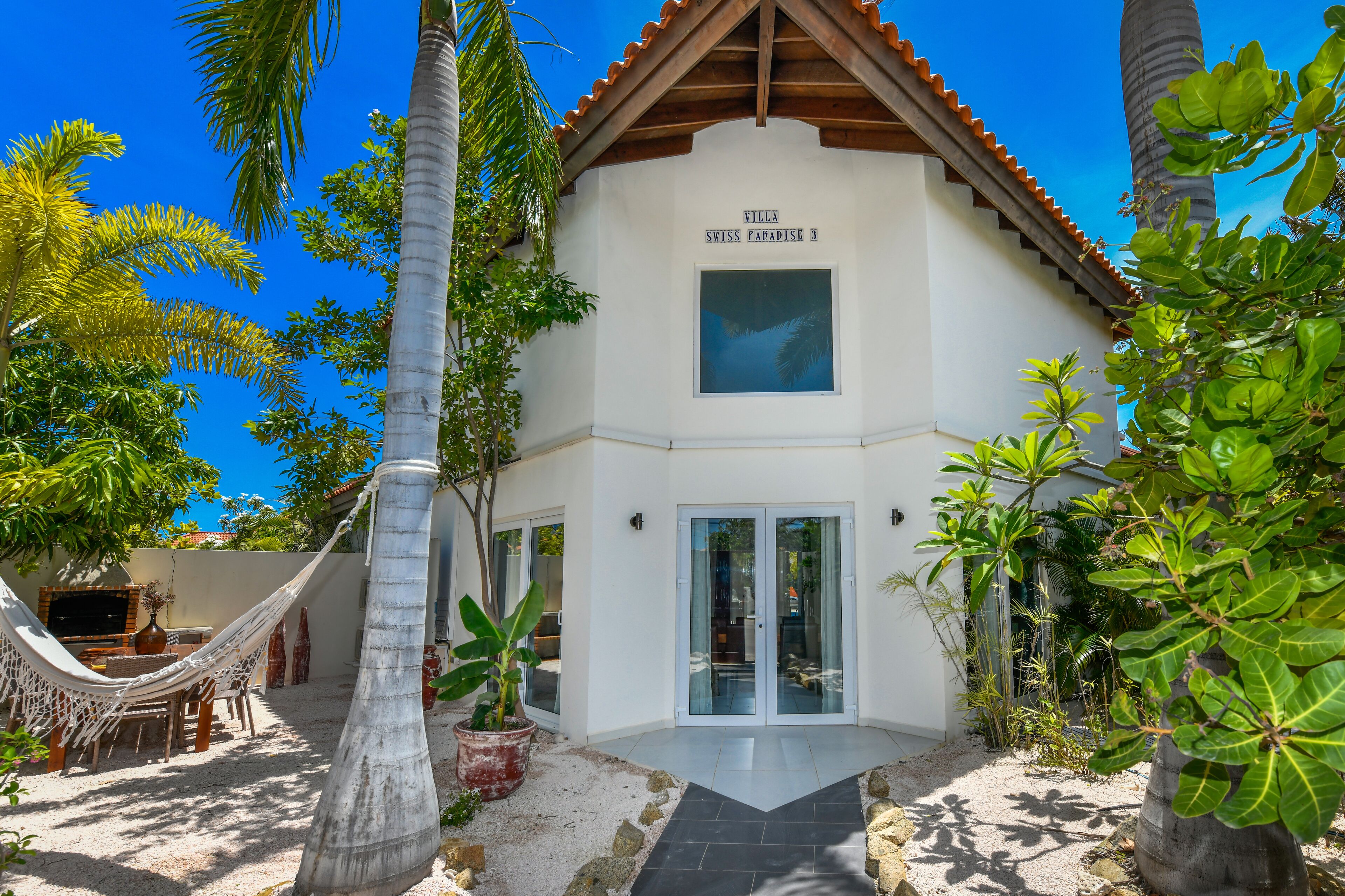 En villa med hvide facader, et trætag og et skilt, der siger "Villa Swiss Paradise".