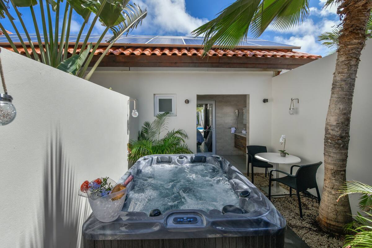 A hot tub in a private outdoor area with a patio, a small table, and chairs.