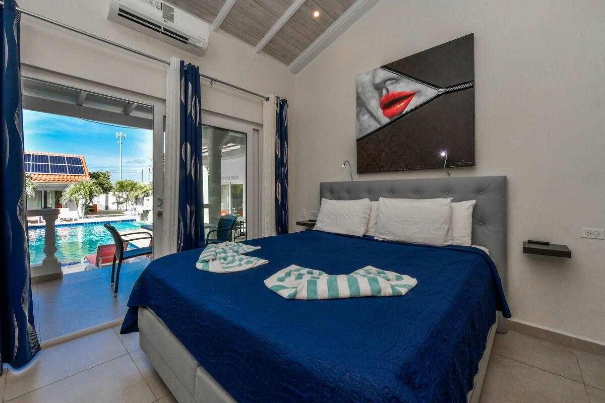 A hotel room with a bed, a view of a swimming pool, and a large window.