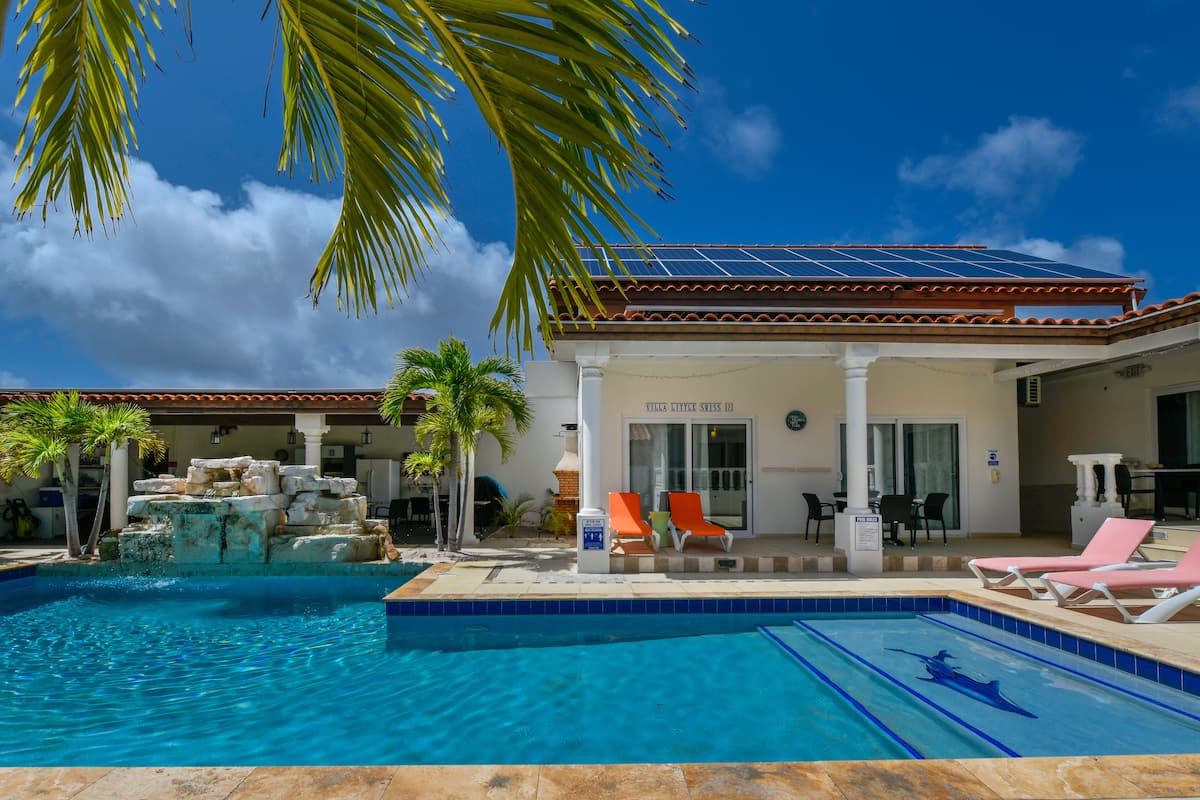 A swimming pool with a rock waterfall, lounge chairs, and a building with a sign reading "Villa Little Swiss."