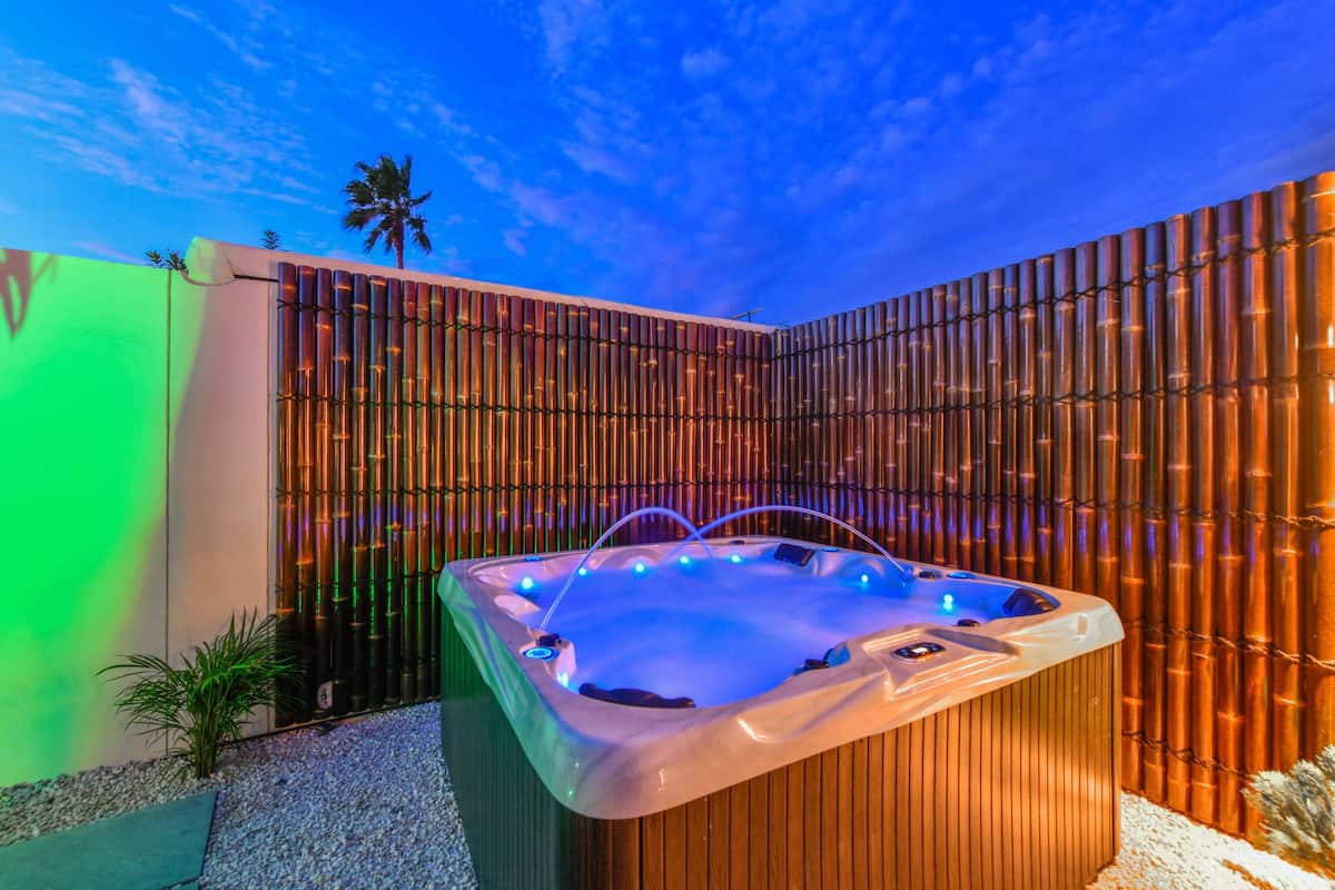 A hot tub with a bamboo backdrop, a palm tree, and a clear sky.